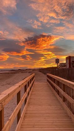 a wooden walkway leading to the beach at sunset with clouds in the sky above it