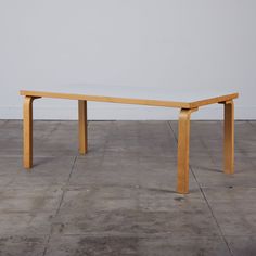 a wooden table sitting on top of a cement floor in front of a white wall