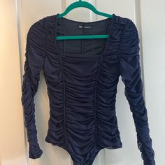 a black bodysuit hanging on a white door with green trimmings and ruffled sleeves