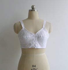 "Brand new vintage deadstock from the 1970's. Soviet era white longline bra top in 100% cotton. Features darted bra cups with circle stitching to the bottom half, slim shoulder straps & a sweet picot trim to the bustline. Closes with a column of buttons to the center front. Could be worn as an undergarment, or even as a cropped camisole top. 100% cotton takes dye well & could be a fun project too! Check out other brassieres in the shop - www.etsy.com/shop/fivestonesvintage?section_id=100 Fitted Cotton Crop Top With Built-in Bra, White Tops With Built-in Bra And Underbust Shape, Fitted Cotton Camisole For Daywear, Summer White Underwire Crop Top, White Underwire Crop Top For Summer, Vintage Fitted Spaghetti Strap Tops, Fitted White Camisole With Removable Bra Pads, Fitted Bra-friendly Tops For Daywear, Vintage Fitted Tank Top With Spaghetti Straps