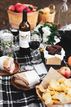 a picnic table with food and wine on it, including bread, crackers, apples, and other snacks