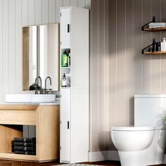 a white toilet sitting in a bathroom next to a wooden cabinet and sink with a mirror above it