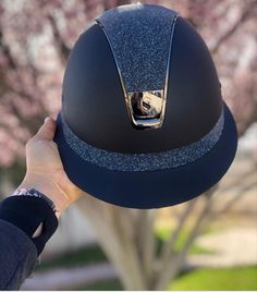 a person holding up a black helmet in front of a tree with pink flowers on it