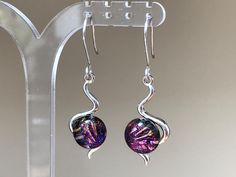 Vibrant deep purple multicoloured dichroic glass drop earrings in a superior silver plated 's' shape setting. The colours of the dichroic stones shift as they moves in the light from purple to hot pink with an abstract pattern of multicoloured colours including gold and green.  The dichroic stones measure approximately 9-10mm in diameter earrings with the setting 18mm long by 12mm wide and the total length of the drop 44mm. They are supplied with a choice of sterling silver 925, hypoallergenic surgical steel or silver plated clip-on ear fittings.  Other complementary jewellery made with this glass is available in other sections ie pendants but please message for more details. The dichroic stones have been handmade in my home studio by cutting and layering 2 sheets of glass and firing in my Modern Purple Earrings For Party, Modern Purple Jewelry For Party, Iridescent Glass Earrings For Gift, Nickel-free Purple Glass Jewelry, Silver Glass Earrings For Party, Round Glass Earrings For Parties, Glass Drop Earrings, Dichroic Glass, Deep Purple