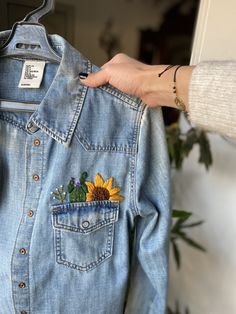 a person holding onto a jean jacket with a sunflower patch on it