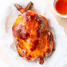 a cooked chicken sitting on top of a white plate next to a bowl of sauce