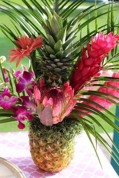 a pineapple vase filled with flowers on top of a pink and white table cloth