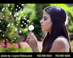 a woman blowing on a dandelion in the park