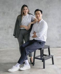 a man and woman posing for a photo in front of a concrete wall with a bench