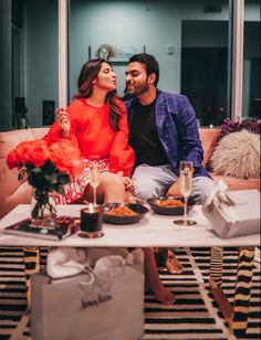 a man and woman sitting on top of a couch in front of a coffee table