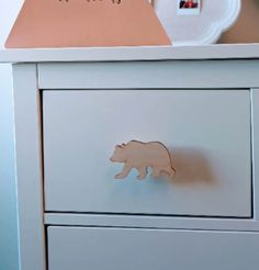 a white dresser with a wooden bear drawer knob on it's front and bottom