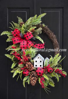 a christmas wreath with red and black plaid bows, pine cones, evergreen leaves, and a white house