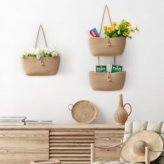 three baskets are hanging on the wall above a couch with flowers and books in it