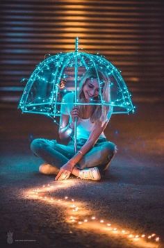 a woman sitting on the ground holding an umbrella over her head with fairy lights around it