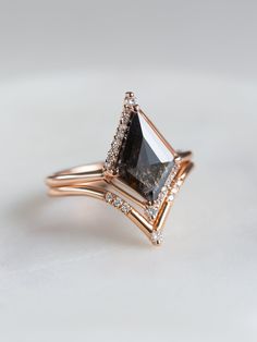 Why You'll Love It ﻿This alternative and geometric inspired ring displays a polished kite salt and pepper diamond that has a perfect mixture of unique inclusions. The center stone is encased in a one-of-a-kind setting with a minimal band and bright petite diamonds to emphasis its beauty. Details 14K solid gold Band width is approx. 1.60mm Salt & pepper kite diamond x 1 piece (Approx. 1.20ct) Size of gem may vary based on our selection for all non-custom engagement rings. SI/G Color White Round 1 Black Stone Ring Engagement, Geometric Engagement Ring, Gothic Wedding Rings, Kite Diamond, Obsidian Ring, Tiny Wedding, Black Engagement Ring, Future Engagement Rings, Solid Gold Band