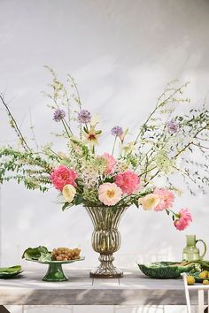 an arrangement of flowers in a vase on top of a table with plates and cups