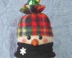 a snowman wearing a plaid hat and scarf with a green ornament on top