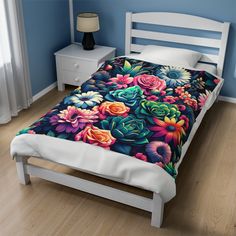 a bed with colorful flowers on it in a blue room next to a white night stand