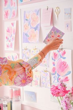 a woman holding up a card in front of a wall covered with cards and flowers