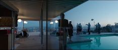 some people are standing near a swimming pool at dusk with the city in the background