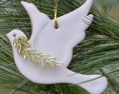 a white ceramic bird ornament hanging from a pine tree