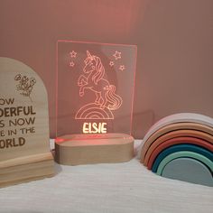 an illuminated unicorn on top of a wooden base next to rainbow coasters and a plaque