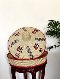 two woven hats sitting on top of a wooden stool next to a potted plant