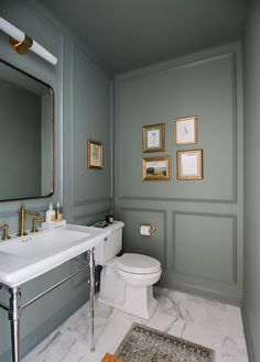 a white toilet sitting next to a sink in a bathroom under paintings on the wall