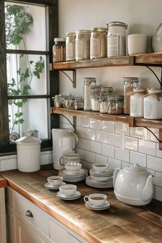 a kitchen counter topped with lots of white dishes and cups on top of wooden shelves