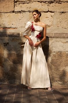 a woman in a white dress standing next to a stone wall with flowers on it