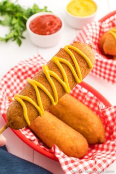 a person holding a hot dog on a stick with mustard drizzled over it