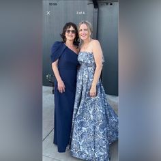 two women standing next to each other on a sidewalk wearing blue dresses and one is smiling at the camera