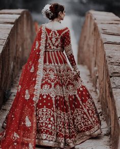 a woman in a red and gold bridal gown standing on a bridge with her back to the camera