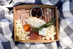 an open box filled with cheese, meat and olives on top of a blanket