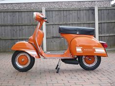 an orange scooter parked in front of a wooden fence