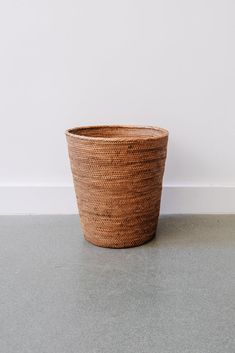 a brown basket sitting on top of a gray floor next to a wall and a white wall