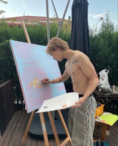 a shirtless man is painting on an easel