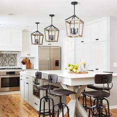 a kitchen island with four stools and three lights hanging from it's ceiling