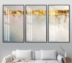 three paintings hanging on the wall next to a couch in a living room with white furniture