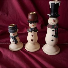 three snowmen are standing next to each other on a red cloth covered tablecloth