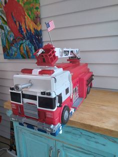 a red and white toy truck sitting on top of a wooden counter next to a painting