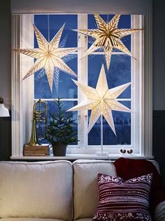 christmas decorations are hanging from the window sill in front of a white couch with red pillows