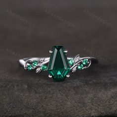 an emerald colored ring with leaves on the sides and green stones in the middle, sitting on top of a rock