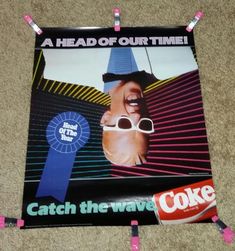 a poster on the floor that says, catch the wave coke and has a head of our time