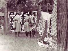 an old black and white photo of people standing in front of a quilted wall