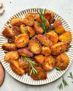 a white plate topped with fried potatoes covered in seasoning and sprinkled with rosemary