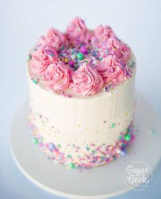 a white cake with pink frosting and sprinkles on the top is sitting on a plate