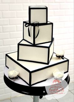 a three tiered cake with white frosting and black trim on a metal stand