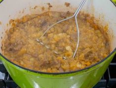 a green pot filled with food and a whisk on top of the stove