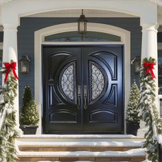 a black front door with two wreaths on the steps and christmas trees around it